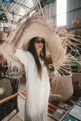 Camisa larga color crudo con cuello camisero, botones frontales y detalles de pliegues verticales en la parte delantera.