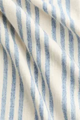 Top halter color beige y azul a rayas, con escote en V pronunciado, tirantes anchos para atar al cuello y detalle de moño ajustable en el centro del pecho. Diseño holgado con leve vuelo en el bajo.