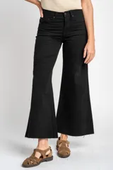Jean de corte wide leg y tiro medio, confeccionado en algodón peinado de color negro. Presenta un diseño de pierna ancha con ruedo deshilachado y cierre frontal con botón y cremallera.