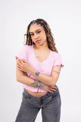 Remera corta de punto canalé color rosa, con escote en V, mangas cortas con volados y cierre frontal con botones.