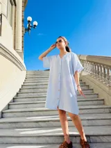 Vestido camisero corto celeste con rayas verticales blancas, cuello en V y botones frontales.