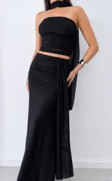 Conjunto negro compuesto por un top strapless drapeado con capa larga trasera y una falda larga fruncida en la cintura con caída lateral.