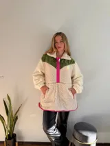 Canguro de polar color crema con bloques de color verde militar en la parte superior y fucsia en los bordes y cierre.