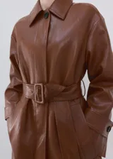 Chaqueta larga de efecto cuero color marrón, con cuello camisero, botonadura frontal oculta, bolsillos laterales y cinturón ajustable con hebilla en la cintura. Cuenta con trabillas en las muñecas y diseño amplio.