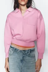 Sweater tipo polo de punto liso, con cuello solapa, manga larga y bolsillo delantero de plastrón. Presenta cierre frontal con botones y puños y ruedo acanalados.