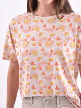 Remera de manga corta color beige con estampado de bananas en tonos amarillo, naranja y rosado.