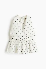 Top halter color blanco con estampado de lunares negros, escote en V pronunciado y detalle fruncido en la cintura con vuelo tipo peplum.