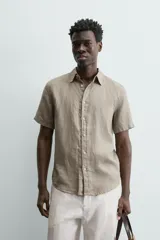 Camisa de lino color beige de corte relajado, con cuello solapa, manga corta y cierre frontal con botones.