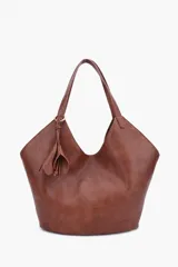 Cartera tote tipo hobo de cuero sintético en color marrón, con diseño de lados angulares, doble asa de hombro y detalle colgante de borla con argolla metálica. Cuenta con el logotipo de la marca grabado en la parte inferior.