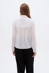 Camisa negra de poliéster con detalles de lurex y textura en relieve, corte holgado, mangas largas con puños y cierre frontal con botones.