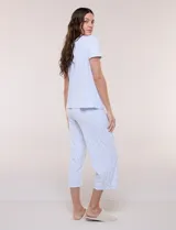 Pijama de dos piezas con estampado floral en tonos azules sobre fondo blanco, compuesto por una remera de manga corta con cuello redondo y botones frontales, y un pantalón capri con cintura elastizada y bolsillos.