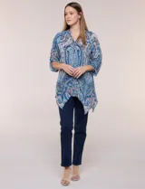 Blusa holgada de poliéster con estampado de arabescos en tonos azules, escote en V con botones frontales, mangas 3/4 y ruedo asimétrico en punta.