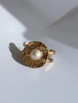 Brazalete rígido de diseño abierto, con una pieza central circular de textura martillada en tono dorado y una perla central.