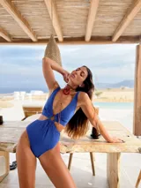 Traje de baño entero color azul, con escote pronunciado en V, aberturas laterales y detalle de argolla de resina en el centro. Presenta una textura sutil en la tela y corte tipo vedetina.