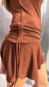 Vestido corto marrón con brillo, de un solo hombro y manga corta caída, con diseño ajustado al cuerpo y falda evasé con detalle de fruncido en la cintura.