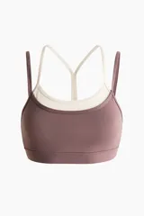 Top deportivo color malva con forro interior en tono crudo, confeccionado en tejido funcional con diseño de doble bretel fino en contraste y copas con relleno extraíble.