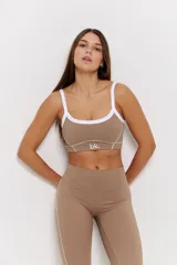 Conjunto deportivo compuesto por un top y un pantalón largo color habano. El top es de escote redondo con breteles blancos y detalle de logo 'bk.' en el frente. El pantalón es de tiro alto con costuras laterales blancas y corte ligeramente acampanado en el ruedo.