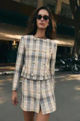 Blazer de cuello redondo y manga larga, con diseño a cuadros en tonos beige, azul y negro. Presenta cierre frontal cruzado con botones metálicos y corte recto.