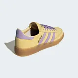 Championes Adidas modelo Handball Spezial, confeccionados en gamuza color amarillo con detalles en lila en las bandas laterales, talón y cordones. Presenta suela de caucho color caramelo y el logo Spezial en dorado en el lateral.