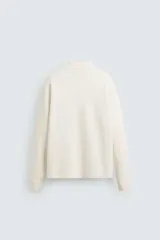 Polo de punto de manga larga con cuello solapa y cierre frontal de botones. Presenta un diseño de corte regular con aberturas laterales en el bajo.