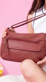 Bandolera morral color tostado con textura de cuero granulado. Cuenta con un bolsillo frontal con solapa y cierre, y otro bolsillo frontal con cierre. Tiene una correa ajustable y un compartimento principal con cierre.