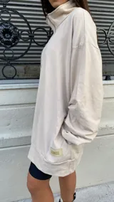 Buzo color beige de algodón con cierre frontal, cuello alto y bolsillo escondido.