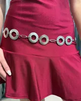 Cinturón de cadena plateado compuesto por eslabones circulares con textura grabada unidos por eslabones rectangulares simples.