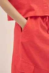 Falda larga color coral, estilo cargo, con cintura regulable con cordón, tajo frontal y bolsillos laterales con solapa.