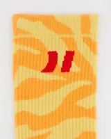 Par de medias de caña media con estampado de rayas estilo cebra en tonos amarillo claro y naranja. Presentan texto rojo bordado en la planta del pie que dice "ART." y un logo rojo en la caña.