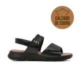 Sandalia casual de cuero Usaflex modelo Ainara, color negro con plataforma baja y plantilla marrón. Cuenta con tiras ajustables con cierre de velcro y el logo de la marca en el empeine.