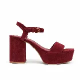 Sandalia de fiesta Dalia color bordó, confeccionada en gamuza de cuero legítimo. Cuenta con diseño de tira frontal ancha, taco ancho, plataforma y pulsera ajustable al tobillo con hebilla metálica.