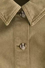 Campera camisera de sarga de algodón verde militar con cuello clásico, cierre frontal de botones y dos bolsillos delanteros de parche. Cuenta con hombros caídos, mangas largas con puños abotonados y bajo recto con aberturas laterales redondeadas.
