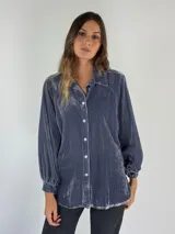 Camisa de terciopelo azul grisáceo, de corte recto, con cuello camisero, cierre frontal con botones y mangas largas abullonadas con puños elásticos.