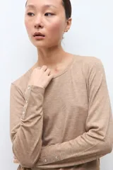 Remera de manga larga color tostado melange, con cuello redondo y detalle de botones metálicos en los puños.