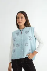 Chaleco de punto color celeste con cierre frontal de botones y diseño bordado de flores en tono gris. Presenta cuello redondo y terminaciones en tejido acanalado.