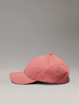 Gorra de béisbol color rosado, confeccionada en sarga de algodón orgánico, con cierre ajustable y herraje metálico con el monograma 'ck' en la parte frontal.