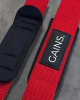 Straps de levantamiento de pesas color negro con logo "GAINS." en blanco.