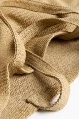Bolso de playa tipo tote de tejido texturizado en color beige, con dos asas superiores para llevar al hombro.