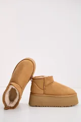 Bota corta tipo ugg en color camel, con plataforma alta y suela dentada. Presenta un diseño de gamuza con interior forrado y tirador en la parte trasera.