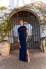 Vestido largo azul marino sin mangas, de corte recto con tajo lateral y diseño strapless con sobrecapa fluida superpuesta.