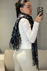Bufanda rectangular con estampado animal print de leopardo en tonos marrones y negros, con terminación de flecos en los extremos.