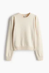 Sweater de punto suave color beige, con cuello redondo, mangas largas con frunces en los hombros y terminaciones acanaladas en cuello, puños y bajo.