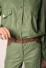 Camisa verde de cuero sintético con cuello marrón, cierre frontal con botones, dos bolsillos con solapa en el pecho y cinturón marrón.