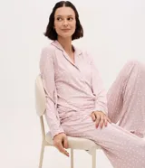Pijama largo estilo americano de color rosado con estampado de lunares blancos, confeccionado en tejido peach touch. Consta de una blusa de manga larga con solapas, cierre frontal de botones y bajo ondulado, y un pantalón largo a juego.