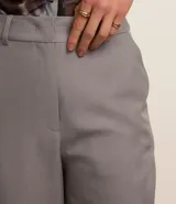 Pantalón de vestir gris oscuro, de corte recto, con bolsillos laterales y traseros. Se ajusta a la cintura con cinturón de cuero marrón.
