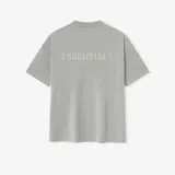 Camiseta gris con logo "Essentials Fear of God" en el pecho y etiqueta de goma en la parte posterior. Corte oversize.