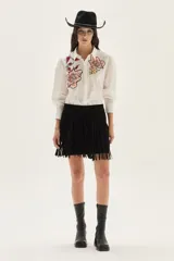 Falda corta negra con flecos largos desmontables que se adhieren a la cintura mediante cierre, confeccionada en cuero.