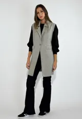 Chaleco largo color beige, con cuello solapa, un botón frontal y dos bolsillos de parche. Presenta costuras decorativas en contraste.