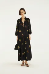 Vestido largo negro de mangas largas con puños elastizados, escote en V con lazo regulable y falda amplia con recorte fruncido, confeccionado en tejido liviano con estampado floral e inspirado en la selva.