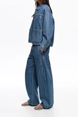 Chaqueta corta de denim en color azul con diseño de rayas verticales blancas, cuello camisero, bolsillos delanteros de parche y cierre frontal con botones metálicos.